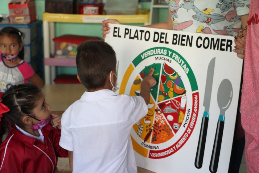 Niño apuntando aun cartel  del plato del bien comer.