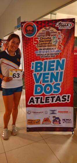 Estudiante de negocios, Yadira Franco, posando al lado del cartel "5to Circuito Nacional de Caminata Coatzacoalcos".