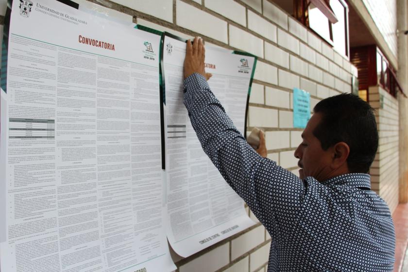 Persona pegando la convocatoria para elegir al próximo Consejo General Universitario.